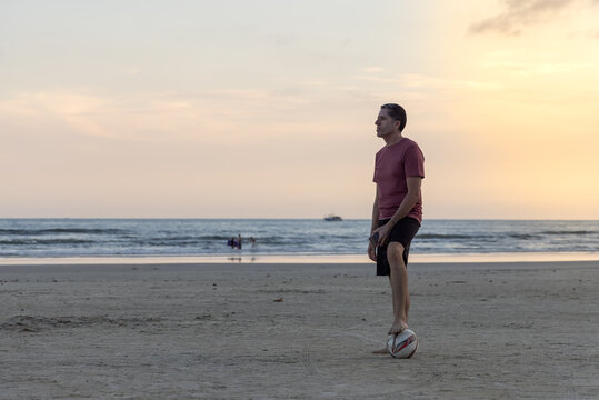 Homem em pé na praia pisando sobre uma bola de futebol
