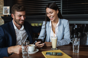 Happy couple man and woman sitting in modern cafe bar or restaurant and drinking coffee.