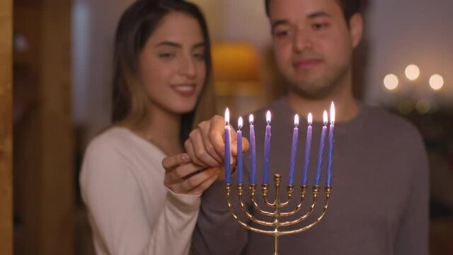 Medium Shot of Young Couple Lighting Candles On Menorah During Hanukkah Celebration