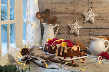 Traditional christmas cinnamon cake decorated with fruits and spekulatius cookies cream on a kitchen countertop.