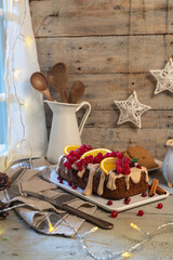 Traditional christmas cinnamon cake decorated with fruits and spekulatius cookies cream on a kitchen countertop.