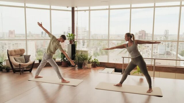 Full shot of young couple having pair yoga training doing stretching exercises in front of each other side bending forward with arm up in modern studio