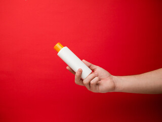 Hand holding white shampoo bottle isolated on red background.