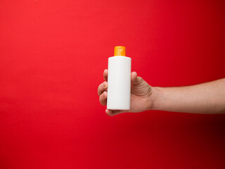 Hand holding white shampoo bottle isolated on red background.