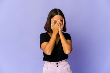 Young mixed race woman blink at the camera through fingers, embarrassed covering face.