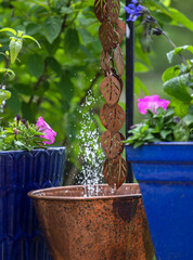 Solar energy pump in a copper planter with a copper rain chain in a garden with blue ceramic pottery