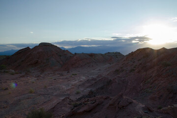 The red canyon and valley at sunset. Panorama view of the arid desert, sandstone formations, rocky mountains, lens flare and hiding sun in Talampaya national park in La Rioja, Argentina.