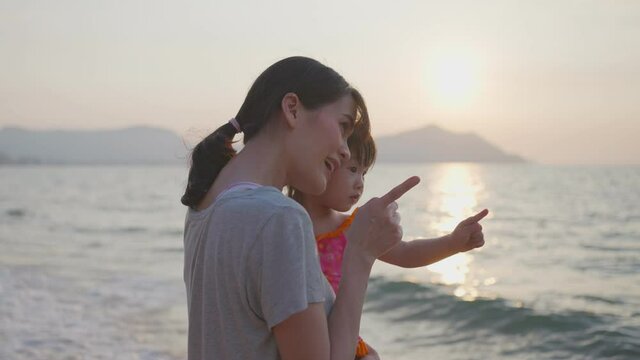 Asian young mother standing on the beach, holding her baby girl in arm
