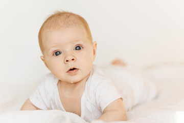 Portrait of adorable baby girl laying on comfortable bed at home, beautiful cute toddler look at the camera with big interest, childhood and childcare concept