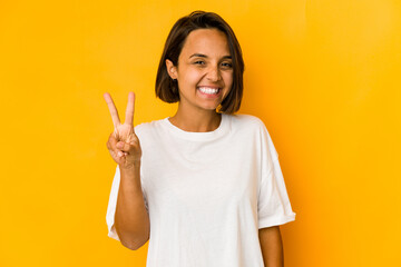 Young hispanic woman isolated on yellow joyful and carefree showing a peace symbol with fingers.