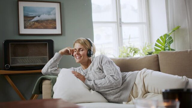 Portrait of woman with closed eyes with headphones relaxing indoors at home, mental health care concept.