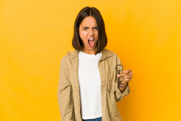 Obraz premium Young hispanic woman holding an old key screaming very angry and aggressive.