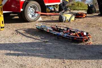 Stokes basket on gravel with climbing gear for cliff search-and-rescue of injured person. Fire truck and ropes in background