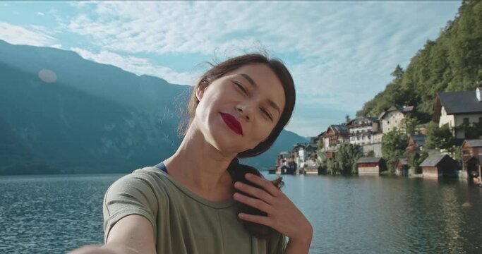 Portrait of happy young woman making selfie in front of magnifficent background. Girl smiling capturing breathtaking view of nature and village. Beautiful sunny day on vacation. concept of travel.