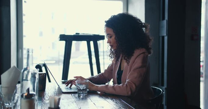 Side view beautiful young multiethnic female student working online, e-learning on internet with laptop at light cafe.