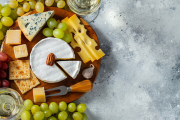 Tasting cheese dish on a wooden plate. Food for wine and romantic date, cheese delicatessen on a light concrete background. Top view with copy space