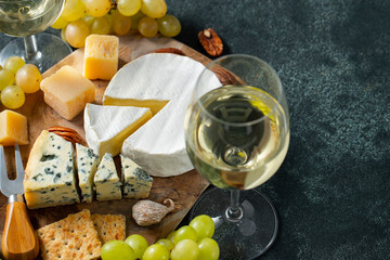 Tasting cheese dish on a wooden plate. Food for wine and romantic date, cheese delicatessen on a black concrete background. with copy space