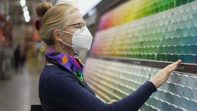 Wide angle view slow motion of woman wearing face mask looking at paint chips in a hardware store. Concept of coronavirus shopping experience.