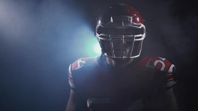 Portrait of determined professional American football player in helmet in dramatic light ready for game. Masculine and agression. Confident man in uniform. Usa team game, extreme sport spirit concept.