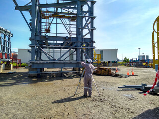 A land surveyor engineer during his work with surveying using theodolite or total station scanner,Inside a mechanical engineering construction site.