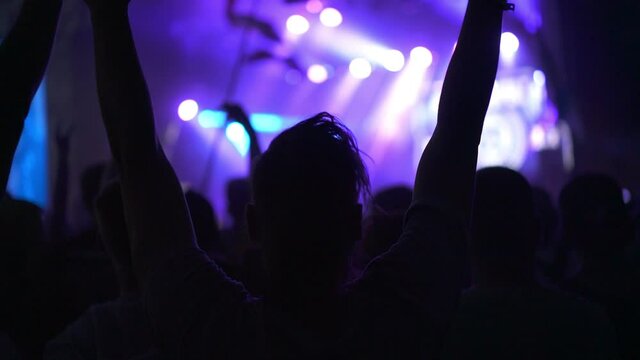 People clapping their hands and singing songs. Silhouette of a girl dancing at a rock band concert. Live performance in a nightclub with fans and stars. Concept of entertainment and background.