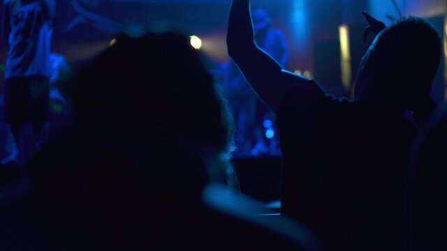 Silhouette of people dancing at a rock band concert. Live performance in a nightclub with fans and stars. People raising their hands and singing songs. Concept of entertainment and background.