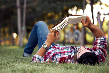 Male white caucasian lying on the lawn reading a book resting.