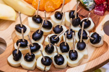 Canapes made of cheese and black olives on the scorched wooden stand on the light blue background