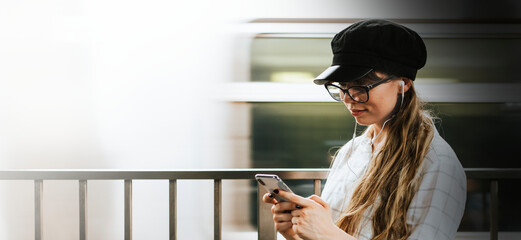 Girl listening to music while waiting for a train at a subway platform