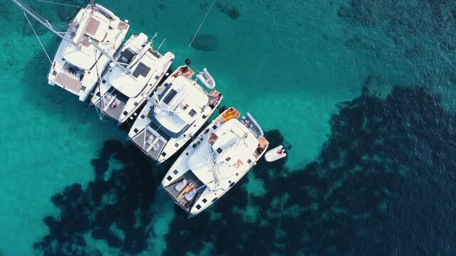 Four yachts anchoring in crystal clear turquoise water while people are working on the boat.