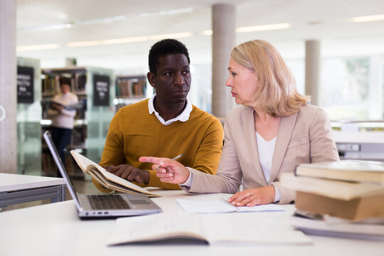 Female teacher working with african-american man in university library. High quality photo