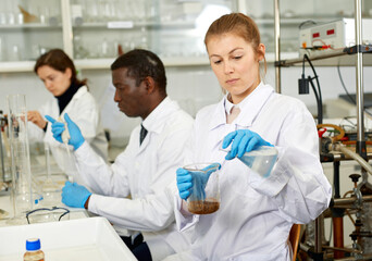 Focused women lab technicians in glasses working with reagents and test tubes, man on background