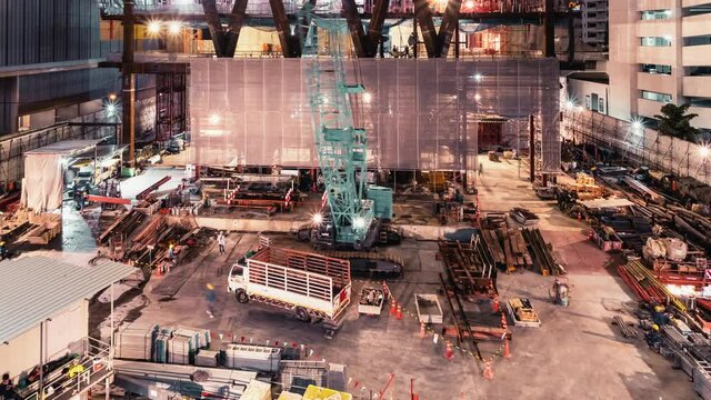 Time-lapse of crane and construction worker in under construction building site at night. Construction industry, industrial business, or civil engineering technology concept. Zoom out