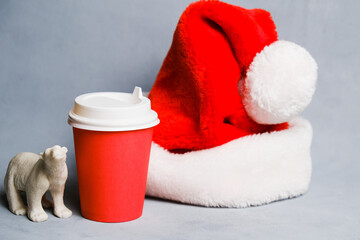 Obraz na płótnie Canvas Keep warm, winter beverage concept. Takeaway coffee container mockup, Santa Claus hat and toy polar bear on grey background. Christmas coffee.