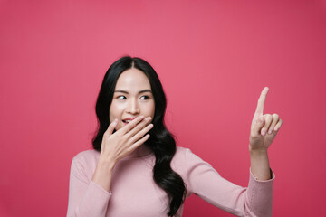 Portrait of asian woman pointing at empty space isolate on pink background.