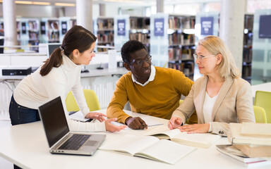 Female tutor helping students preparing for exam in library. High quality photo