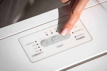 Woman turning on air dryer, purifier, dehumidifier, humidity indicator, air ionizer or water...