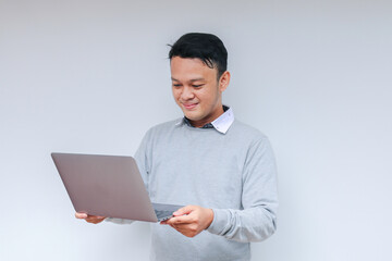 Young Asian man feeling happy and smile when standing and work laptop. Indonesian man wearing grey shirt