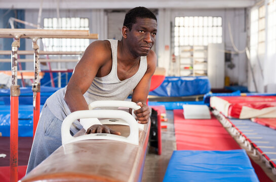 Adult afro man in sportswear doing exercises on gymnastic equipment in acrobatic hall