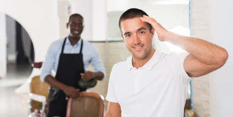 Obraz premium Portrait of cheerful young man satisfied with service in professional barbershop..
