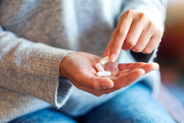 Closeup image of a woman holding and picking white medicine capsules in hand