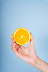 Woman hand holding a slice of orange on blue background.