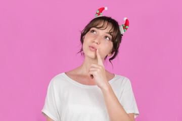 Girl with Christmas decorations in hair and a medical mask on an isolated pink background is...
