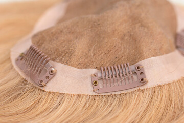 Closeup of snap-comb or wig clips on a light brown toupee.