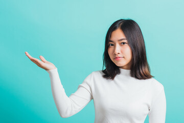 Fototapeta premium Young beautiful Asian woman smiling makeup showing product on blank hand, Portrait female demonstrate presenting something on hand, studio shot isolated on a blue background