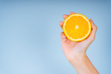 Woman hand holding a slice of orange on blue background.