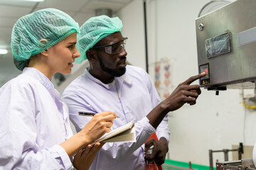 A quality supervisor or food technician explains the use of the Shrink Tunnel Machine to the new employee. Quality inspectors work together in the food factory to inspect food quality in standards. - Powered by Adobe