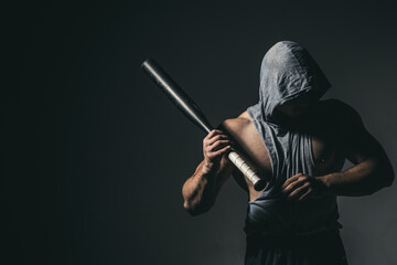 Dangerous man in the mask with baseball bat ready for fight. An aggressive muscular hooded man is...