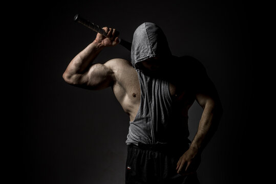 Dangerous muscular man in the mask with baseball bat ready for fight. An aggressive hooded man is holding a baseball bat on black. - Powered by Adobe