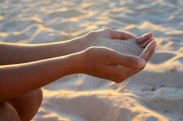 Young woman holds sand in her hands, at sunset